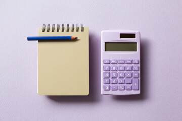 Beige notepad and calculator isolated on purple background. top view, copy space - obrazy, fototapety, plakaty