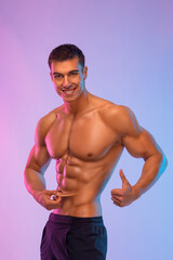 Happy man athlete shows how little subcutaneous fat is in his body. Sportsmen isolated on color...