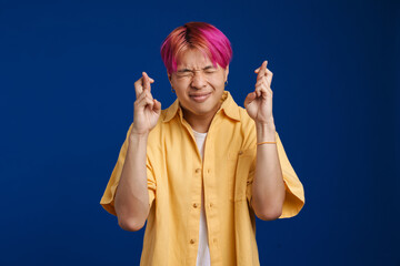 Asian boy with pink hair holding fingers crossed for good luck