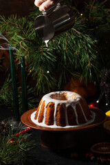 a round cupcake on a dark background is poured from a saucepan with white icing on top