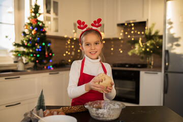 Little beautiful girl in red apron bakes christmas cookies, homemade cakes for christmas