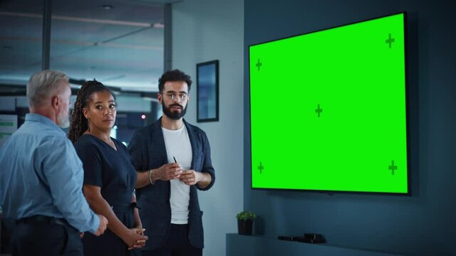 Company Operations Manager Holds Meeting Presentation for a Team of Executives. Adult Male Uses Wide TV Set with Horizontal Green Screen Mock Up Display. People Work in Business Office.