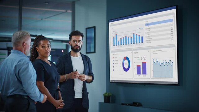 Company Operations Manager Holds Meeting Presentation for a Team of Economists. Adult Male Uses TV Screen with Growth Analysis, Charts, Statistics and Revenue. People Work in Business Office.