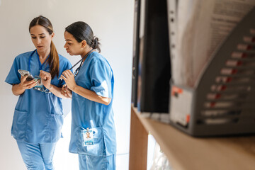 Multiracial women doctors talking and using cellphone in office