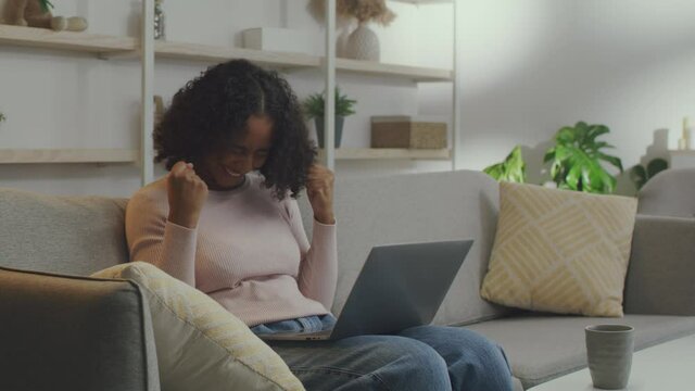 Online win concept. Young cheerful african american lady networking on laptop and reading great news at home, free space