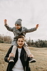 Father holding son on his shoulders, outdoors, in a park.
