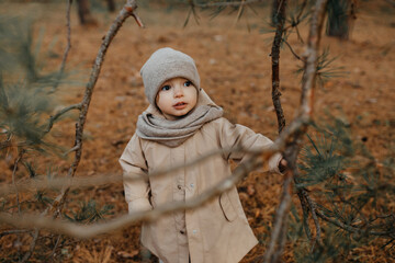 Little girl walking in a park on late autumn day, wearing knitted hat and scarf.