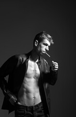 Portrait of a rebel type guy in classic leather jacket with cigarette in mouth against dark...