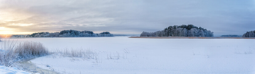 Panorama of snowy winter landscape. Trees are covered with snow and frost. The sea is frozen and allows skiing on it. A cold winter afternoon at sunset in Naantali, Finland.