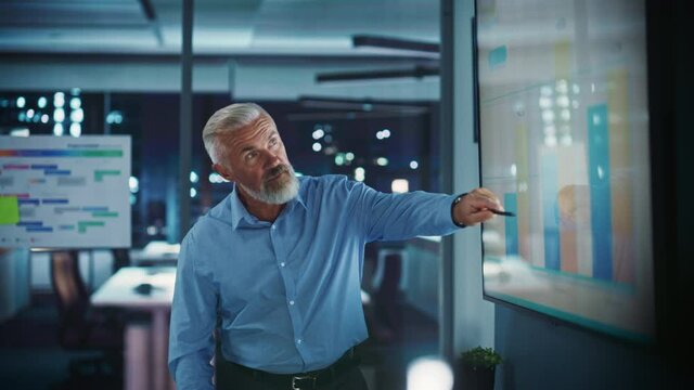 Company Operations Director Holds Sales Meeting Presentation for Employees and Executives. Senior Adult Male Uses TV Screen with Growth Analysis, Charts, Ad Revenue. Work in Business Office.