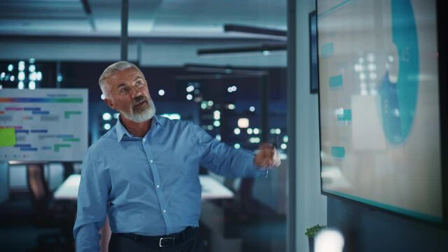 Company CEO Holds Sales Meeting Presentation for Employees and Executives. Senior Adult Male Uses TV Screen with Growth Analysis, Charts, Ad Revenue. Work in Business Office.