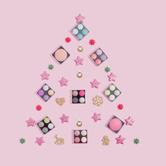 Creative Charistmas and New Year concept. Christmas tree made of makeup cosmetics and ornaments on pink background. Makeup artist Christmas greeting card.