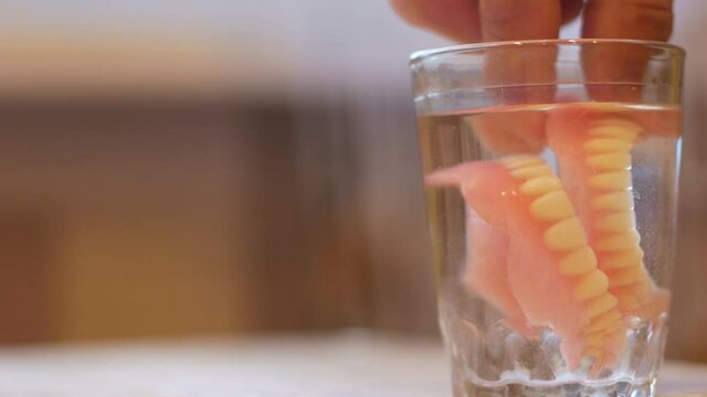 Close-up of a glass with water in which dentures are placed false teeth. Dental implants theme. Dental services. Retired tooth loss false jaw. selective focus
