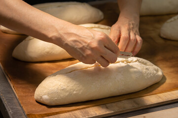 Close-up of a baker's female hands cutting a loaf of dough into a loaf of bread with a blade before baking in the oven. Craft craft bread production