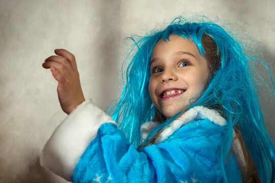 Smiling girl in a blue wig and snow maiden costume on a gray background. Close-up.