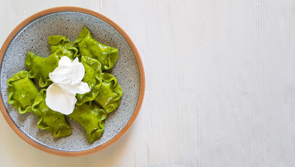 Green dumplings with cottage cheese, spinach and sour cream on ceramic plate on white background