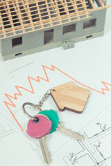 Keys with home shape and downward graphs on construction diagrams of house. Real estate crisis....