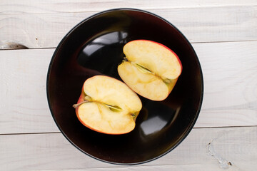 Two half sweet red apples in a ceramic plate on a wooden table, close-up, top view.