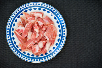 Plato azul, con lonchas de jamón ibérico, sobre fondo negro, vista superior