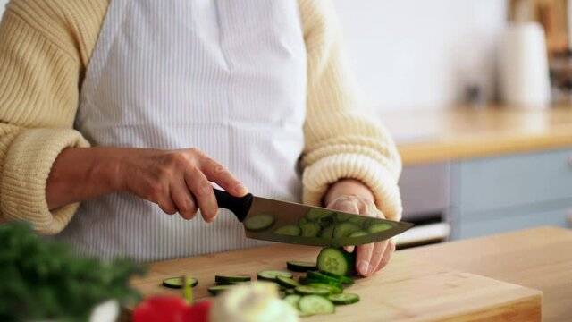 healthy eating, food cooking and culinary concept - hands of senior woman with knife chopping cucumber on kitchen