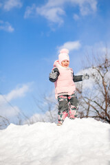 Fototapeta na wymiar Little girl is playing against blue sky. Child has fun on sunny winter day in nature, plays and rides snow slide, jumps on snowdrifts, winter landscape, winter snow forest.