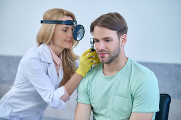 Woman examining mans ear through frontal reflector