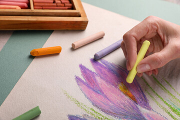 Woman drawing beautiful crocus flowers with soft pastel at table, closeup