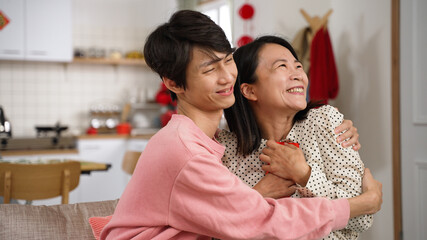 Obraz na płótnie Canvas closeup of considerate chinese son giving lucky money and hugging his happy mother who's holding the envelope near her chest on chinese lunar new year at home