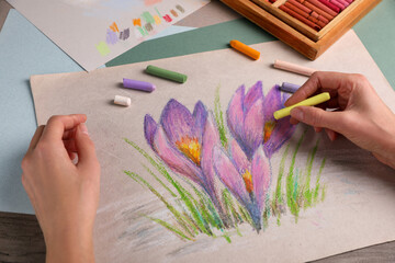 Woman drawing beautiful crocus flowers with soft pastel at wooden table, closeup