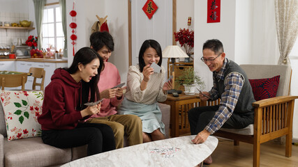 asian family taking turns discarding card on table while playing poker during spring festival at home. excited mother talking with gestures. chinese text translation: spring and congratulations