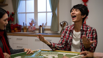 excited son clothing shouting with finger pointing and cheering punching air with fist for winning mahjong game and asking money with beckoning gestures at home during spring festival - obrazy, fototapety, plakaty
