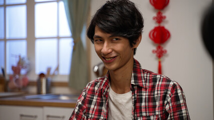 closeup of a scheming son man plaid shirt looking around at his components with cunning smile on face in mahjong game on chinese lunar new year's eve at home