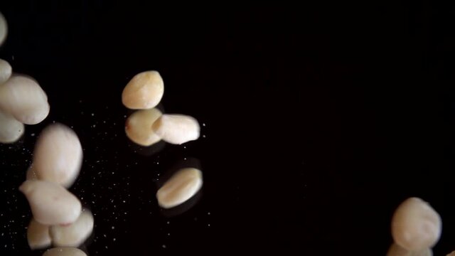 Nuts. Raw blanched peanuts fall on a black mirror surface. Slow motion.
