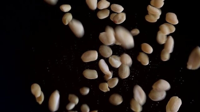 Nuts. Raw blanched peanuts fall on a black mirror surface. Slow motion.