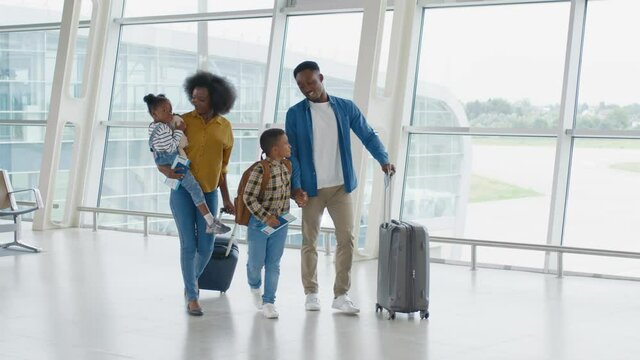 Happy young African American family with two children go on vacation and walk around the airport with suitcases, preparing to board the plane.