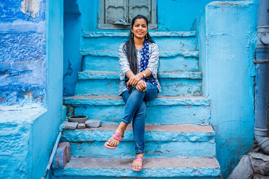 Beautiful Indian female model at blue district Chandpole of the old city in Jodhpur, Rajasthan, India. Attractive girl with long hair in modern clothes, blue jeans and blue background. 