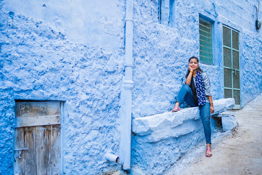 Beautiful Indian female model at blue district Chandpole of the old city in Jodhpur, Rajasthan, India. Attractive girl with long hair in modern clothes, blue jeans and blue background. 