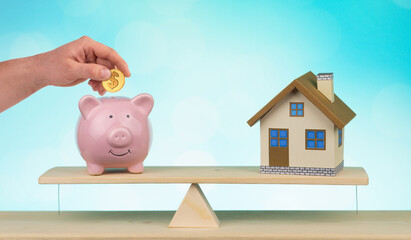 wooden home and piggy bank with hand hold gold coin Us dollar sign put on the scales with balance saving or loan for buy new house or plan business investment concept.