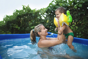 Mom plays with a naked baby in oversleeves in the pool against the background of a summer sunset