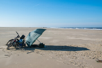 Fototapeta na wymiar Spaziergang am Sandstrand der Nordseeinsel Borkum mit seinem gesunden Reizklima. Schirm als Sonnenschutz und Fahrrad am Strand.