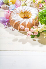 Traditional spring holiday Easter round cake topped with powdered sugar. On light wooden background with sunlight, Easter eggs, decor and spring branches