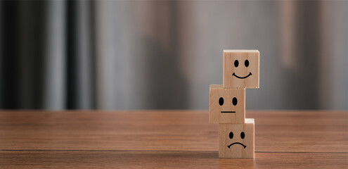 Close up Hand holding of Happy icon on cube blocks about service rating feedback of survey from customer. Business annual satisfaction survey concept. Many sad or happily on wooden table. copy space