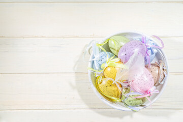 Easter painted colorful pastel eggs in a basket, with feathers on a light wood background. Easter greeting card composition, spring holiday still life background