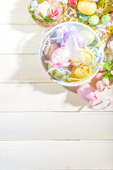 Easter painted colorful pastel eggs in a basket, with feathers on a light wood background. Easter greeting card composition, spring holiday still life background
