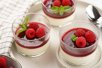 Italian dairy dessert panna cotta with raspberry jam, fresh raspberries and mint on round concrete tray
