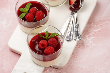 Italian dairy dessert panna cotta with raspberry jam, fresh raspberries and mint on marble board on pink surface
