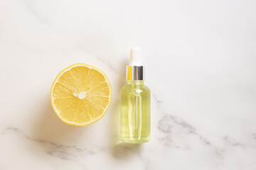 Serum with vitamin C. Lemon essential oil. Glass bottle with a pipette, half a lemon on marble background. Health and beauty concept. Organic natural cosmetics.