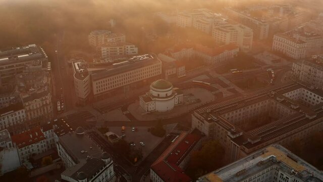 Aerial shot of church at Three Crosses Square. Golden morning sun glowing into mist. Fly above town. Warsaw, Poland
