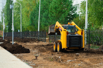 Mini tractor with a bucket at work on a construction site. Small Yellow Backhoe Loader