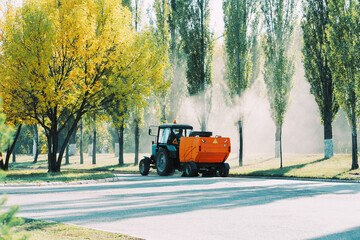 Orange vacuum sweeper towed by a blue tractor removes dust and debris from the roads
